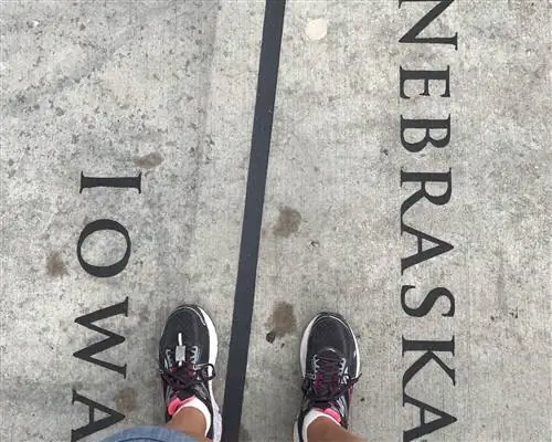 Вид сверху вниз на две ноги, стоящие на бетоне, на линии с надписью Айова слева и Небраска справа.