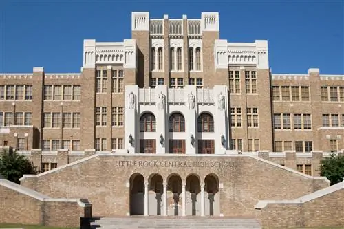 Кирпичный фасад Центральной средней школы Литл-Рока с рядом из четырех больших статуй над дверями и фреской с изображением тигра под ступенями.