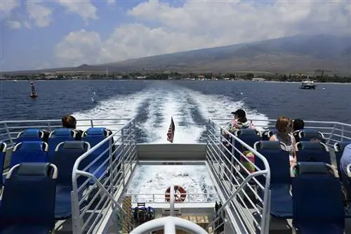 Кадр с задней части парома с несколькими пассажирами, наблюдающими за исчезающим вдалеке вулканическим островом.