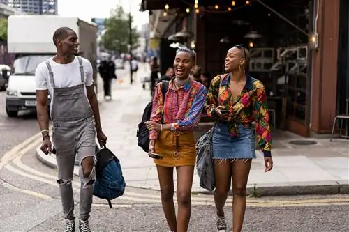 Две женщины и один мужчина вместе идут по улице Лондона, улыбаясь и смеясь.