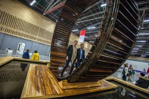 Мужчина и женщина ходят по чему-то похожему на гигантское колесо для хомяка на художественной выставке.