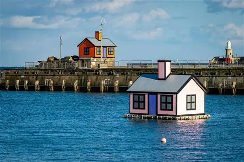 Две инсталляции небольших домов - один плавает на платформе в гавани; другой сидит на рукаве гавани