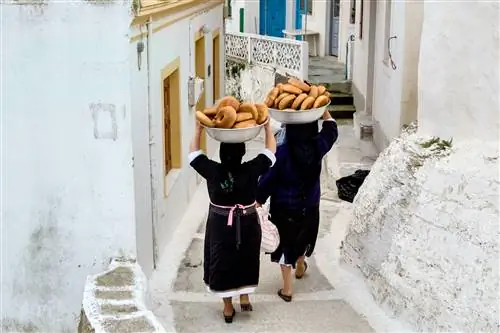 Женщины несут миски с хлебом для празднования греческой православной Пасхи по узкой улочке в Олимпосе на острове Карпатос, Греция.