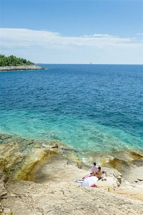 Пара сидит на белых скалах, плавно спускающихся в бирюзовое море.