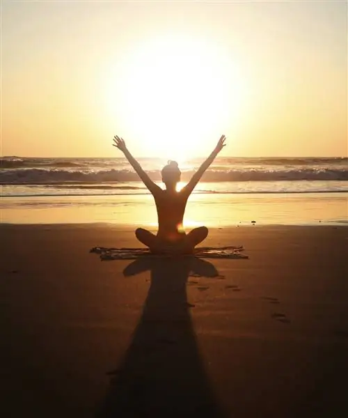 Женщина занимается йогой на пляже на закате