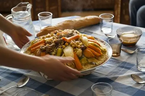 Традиционная марокканская домашняя тарелка кускуса на синем квадратном столе, обслуживаемом динамичными женскими руками со стеклянными ложками и молоком Лабана.