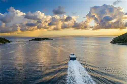 Паром плывет по морю с островами и закатом вдалеке