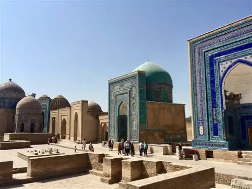 Голубые купола и кафельные фасады вдоль глиняной дорожки, на которой посетители смотрят вверх.
