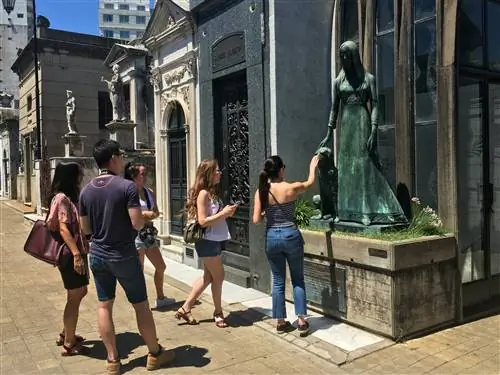 Туристы, прогуливаясь по кладбищу Реколета в Буэнос-Айресе, останавливаются, чтобы полюбоваться скульптурой на фасаде мавзолея.