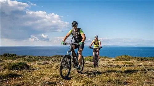 Несколько маршрутов EuroVelo проходят по Хорватии: здесь мы видим молодую пару на горных велосипедах, которая едет по травянистому мысу, а за ним синее море.