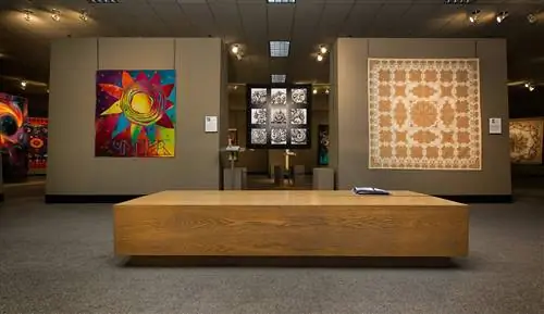 Общий вид галереи Национального музея лоскутного шитья с современным, ярким и абстрактным стеганым одеялом, висящим рядом с традиционным узором в нейтральных тонах.