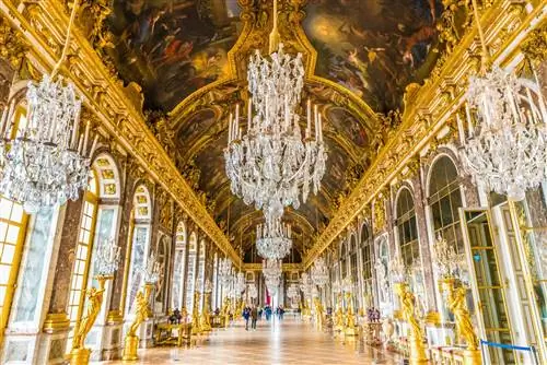 Интерьер Château de Versailles: чрезвычайно величественный коридор с золотыми статуями, огромными окнами и богато украшенными хрустальными люстрами, свисающими с потолка. Интерьер Château de Versailles: чрезвычайно величественный коридор с золотыми статуями, огромными окнами и богато украшенными хрустальными люстрами, свисающими с потолка.
