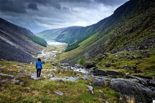 Особенности - Женщина смотрит на долину Глендалох вдоль прогулки по долине Гленеаоло в горах Уиклоу, Ирландия, ненастный весенний день.