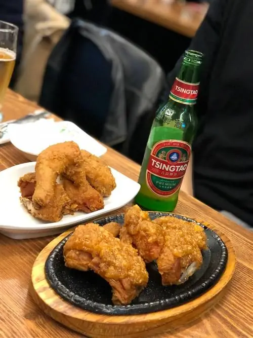 Курица на черном шипящем блюде рядом с бутылкой пива Циндао на деревянном столе