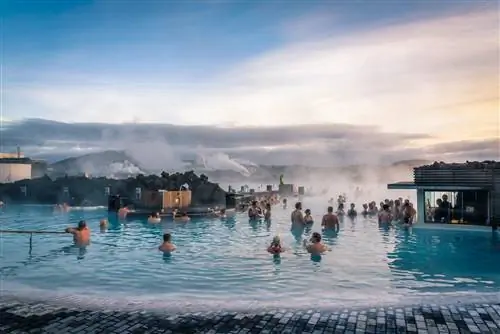 Голубая лагуна в Исландии, геотермальный курорт, на фото много людей, окружающих бар у кромки бассейна.