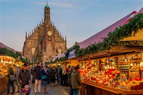 Люди идут по освещенной рождественской ярмарке перед искусно выполненной церковью.