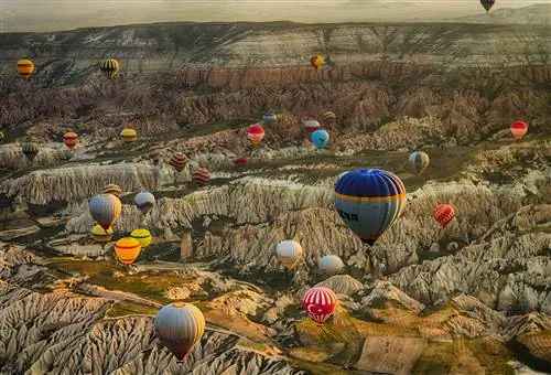 Аэрофотосъемка ярких воздушных шаров над пейзажем с множеством холмов, обнаженных скал и других геологических объектов.