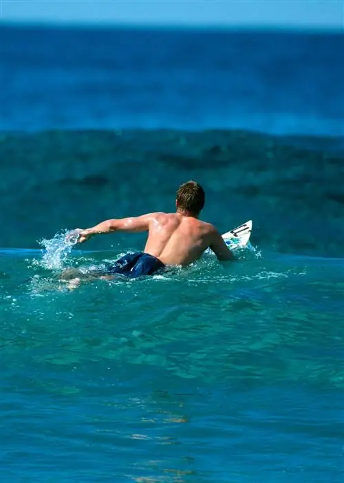 Серфер уходит от пляжа навстречу волнам.