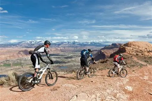 Три человека едут на велосипеде по горному хребту в Моаве, вдалеке видны красные скалы.