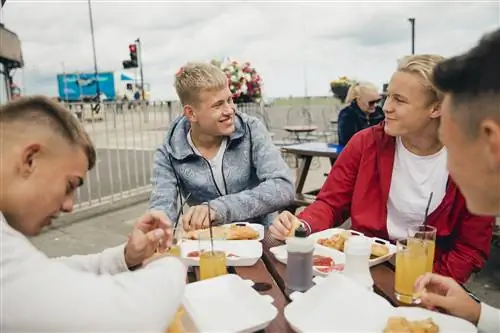 Группа мальчиков-подростков, наслаждающихся рыбой с жареным картофелем после веселого активного дня, проведенного на морском каяке.