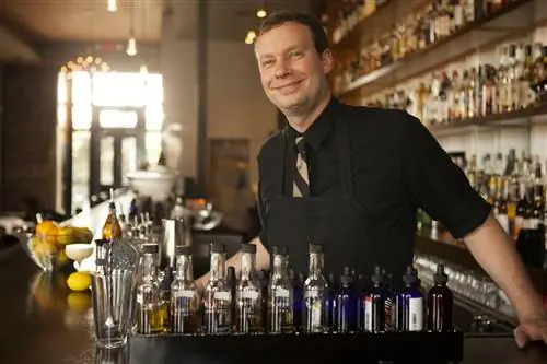 Портрет улыбающегося бармена в баре Cure в Новом Орлеане с бутылками, обшитыми деревянными панелями.