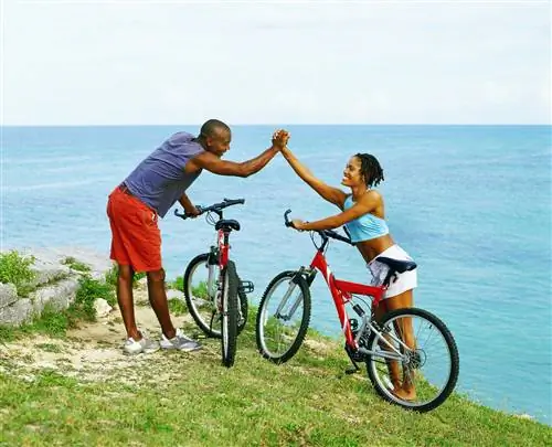 Пара празднует поездку на велосипеде на вершину зеленого холма с видом на море на Бермудских островах.