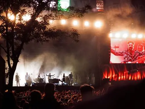 Шантель и Bocovina Orkestar выступают с живым концертом во время Монреальского джазового фестиваля ночью и залиты красным светом с деревом слева от сцены.