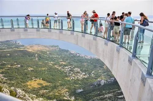 Туристы наслаждаются видами со стеклянного смотрового моста Skywalk Biokovo над горами и Адриатическим морем, Макарска, Хорватия