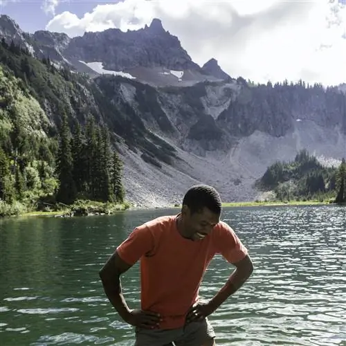 Счастливый мужчина улыбается, бродя по холодному высокогорному озеру в национальном парке Маунт-Рейнир, штат Вашингтон, США.