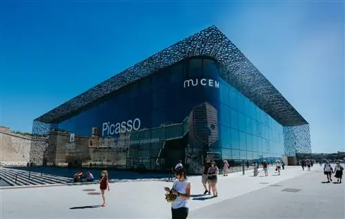 Большой фасад MuCEM из стекла и стали, мимо которого проходят люди.