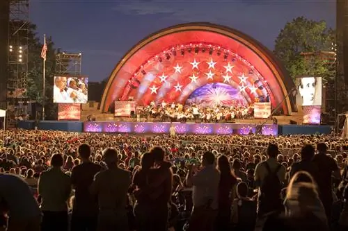 Толпа людей наблюдает за ярко раскрашенной сценой во время выступления Boston Pops в Hatch Memorial Shell в Бостоне.