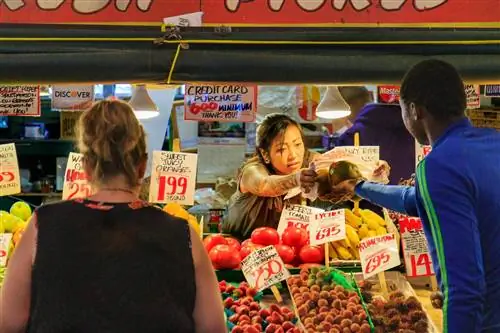 Женщина, работающая в рыночном прилавке, передает продукты покупателю.