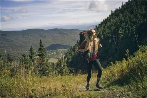 Женщина с большим рюкзаком идет по травянистой тропе на горе Мэнсфилд в Вермонте.