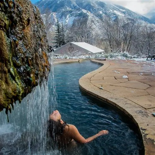 Женщина откидывается назад в водопад природного горячего источника в Avalanche Ranch Hot Springs, Колорадо, США.