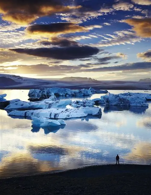 Солнце садится над водным путем, усеянным большими глыбами льда, ощущение перспективы дает только один человек, вырисовывающийся на пляже.