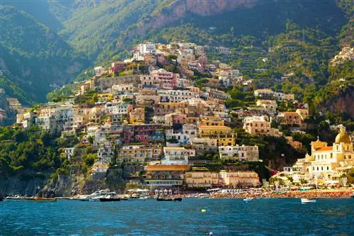 Красочные дома покрывают крутой прибрежный склон, являющийся частью города Позитано на Амальфитанском побережье, Италия. Фотография сделана с моря, а лодки пришвартованы в воде у берега.