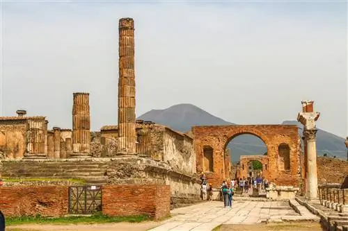 Разрушенный город Помпеи. Люди ходят по развалинам бывшего города, разрушенного Везувием. Вулкан виден на заднем плане изображения.