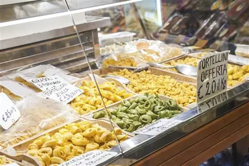 Магазин в Болонье, где продается большое количество пасты, в том числе тортеллини и тортеллони. Паста отображается рядом с ценами, написанными на итальянском языке.
