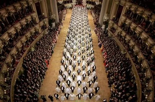 Вид сверху на Венский оперный бал: мужчины, одетые в черное, и женщины, одетые в белое, создают крест-накрест на большом танцполе грандиозного зала.