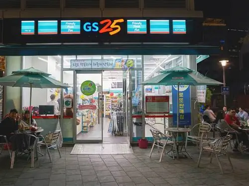 Круглосуточный магазин GS25 ночью, за столиками посетителей, выпивающих перед входом. В большинстве корейских круглосуточных магазинов есть столики, за которыми можно задержаться и выпить до поздней ночи.