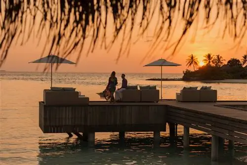 Пара на причале наблюдает за красочным закатом в курортном отеле Four Seasons Resort Maldives в Куда Хураа.