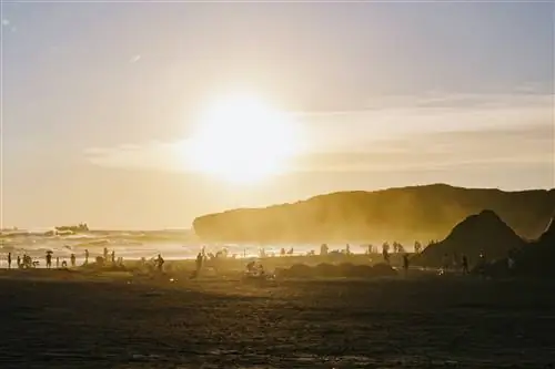 Толпы на пляже вырисовываются силуэтами, когда солнце садится, окрашивая небо оранжевыми полосами.