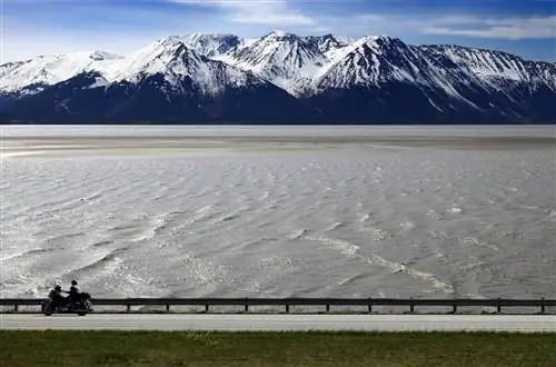 Человек на мотоцикле едет по воде Тернагейн-Арм во время поездки по Аляске.