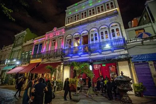 Фотография красочного фасада Rio Scenarium, освещенного синими, розовыми и зелеными огнями, когда гуляки идут к главному входу.