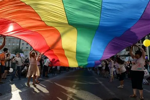 Участники поднимают гигантский радужный флаг над улицей во время ежегодного гей-парада в центре Афин.