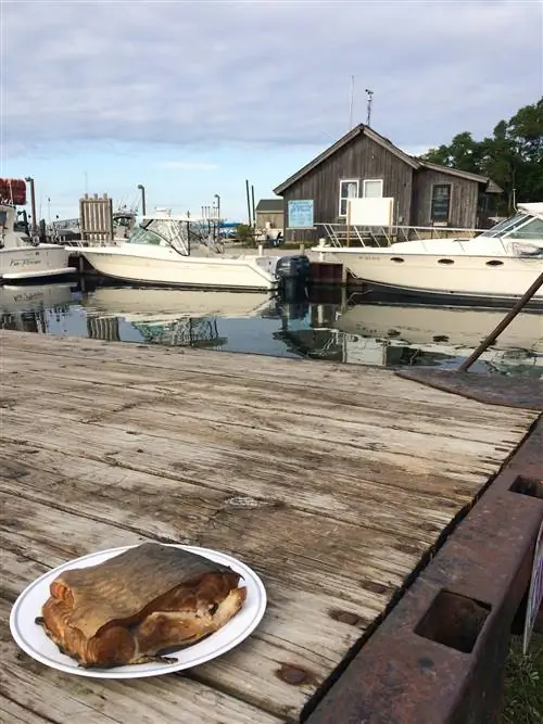 Тарелка с копченой рыбой стоит на причале с лодками и рыбацкими лачугами на заднем плане