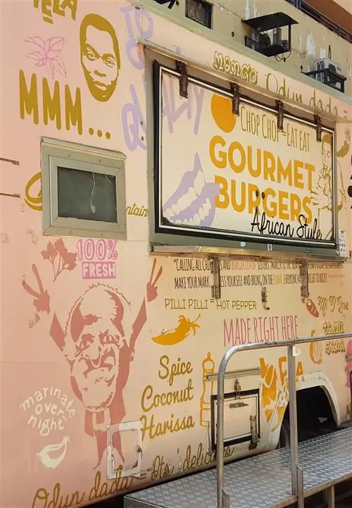 Грузовик с едой Mama Rocks стоит с закрытым служебным окном. Задняя часть грузовика покрыта монохромными изображениями и текстом, напоминающими о таких блюдах, как изысканные гамбургеры.