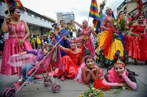 Группа людей, одетых в розово-красные платья, держит флаги прайда в Боготе.