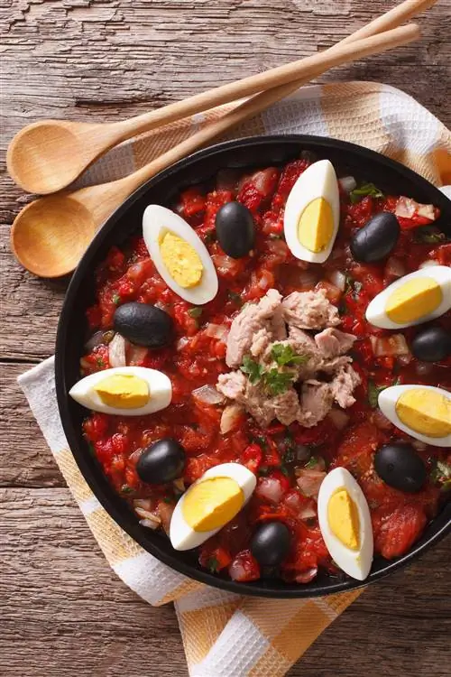 Салат Mechouia (slata mechouia) с овощами, тунцом и яйцами в черной миске на деревянном столе