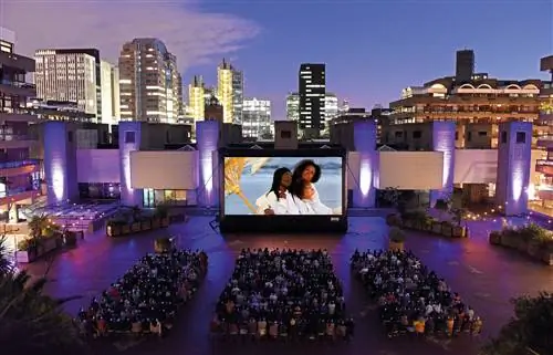 Люди смотрят фильм на большом экране в сумерках в кинотеатре Barbican Outdoor Cinema